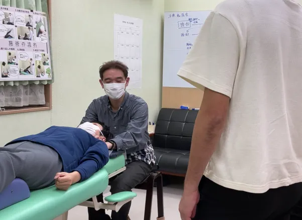 院長が施術をしている様子、近くに施術スタッフがいて話を聞く様子