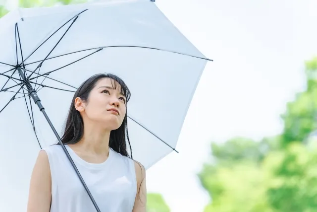 梅雨の日。傘をさしている、なんとなくだるい女性の写真。
